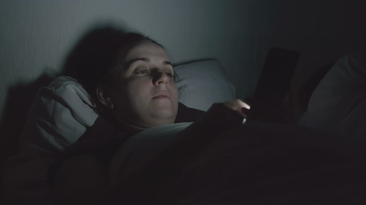 晚上躺在床上用智能手机的女人视频素材