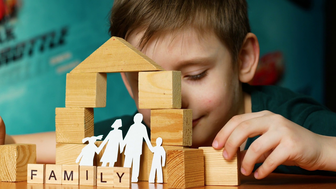 一个7岁的白人男孩用木块搭建了一个玩具房子，上面写着“家庭”，一个用纸剪出的家庭剪影。孩子的梦想是拥有一所房子和一个大家庭。有选择性的重点视频下载
