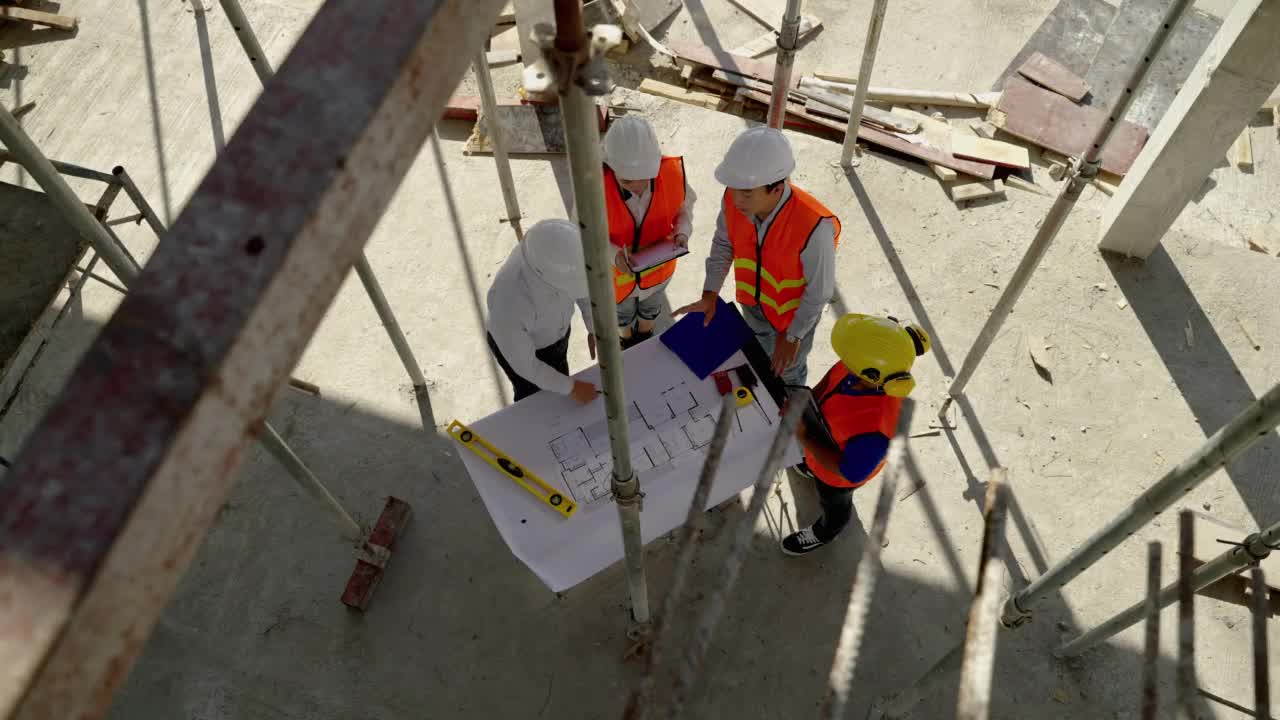 俯视图角，土建团队在施工现场与建筑师、工头一起观看蓝图，规划建筑施工。视频素材