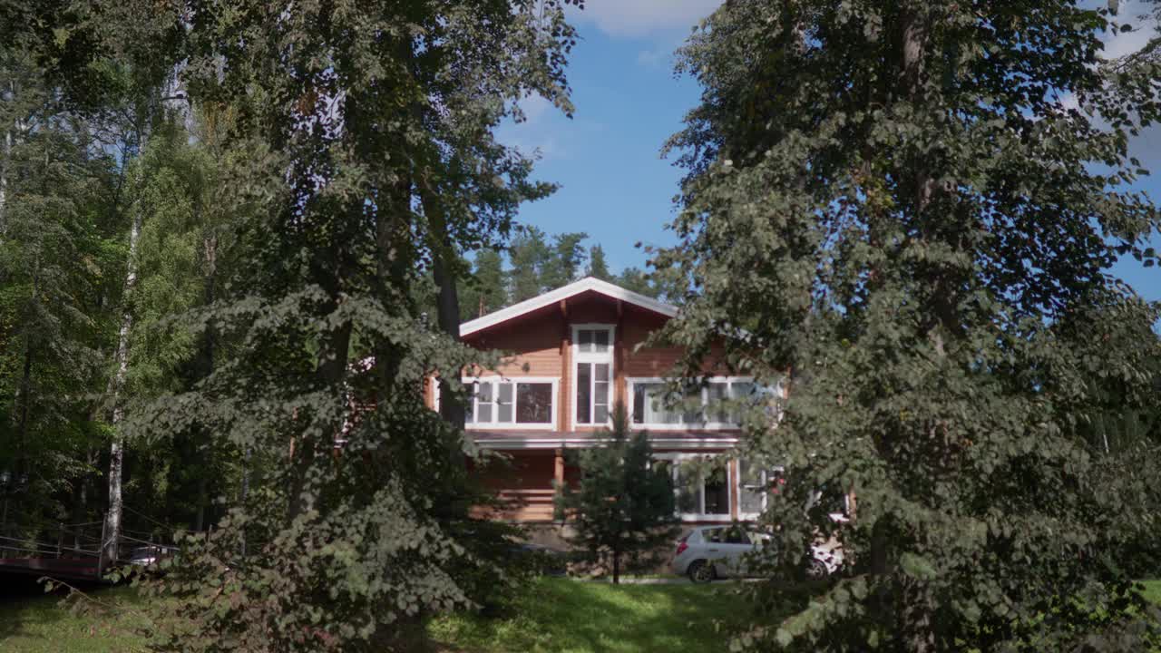 美丽的两层木房子在夏天的一个阳光明媚的日子里在森林里。视频素材