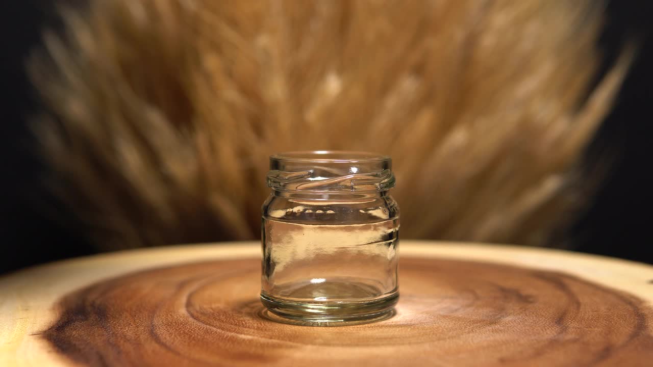 蜂蜜倒在玻璃罐里，宏观特写。滴在木桌或树干上的棕色液体蜂蜜。流动的枫糖浆或糖浆。有机健康高能量食品。有选择性的重点。视频下载