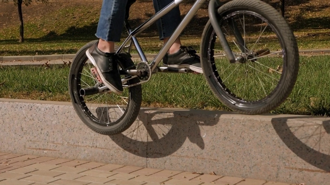 一个运动健将在公园里骑着小轮车特技自行车，他跳到了路边。视频下载