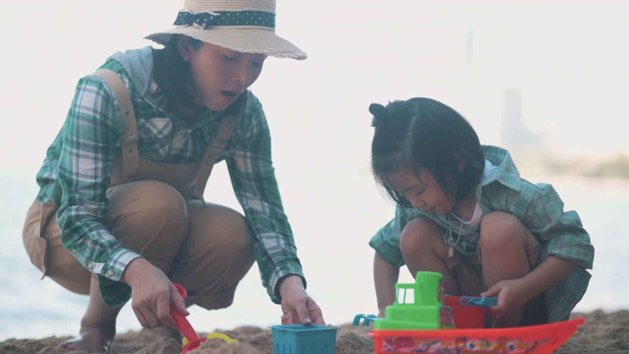 亚洲妈妈和儿子在沙滩上玩玩具视频素材