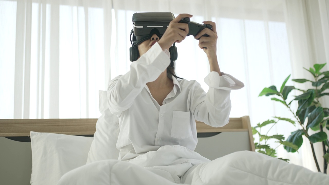 一名年轻女子戴着虚拟现实眼镜玩游戏。她呆在卧室里。视频下载