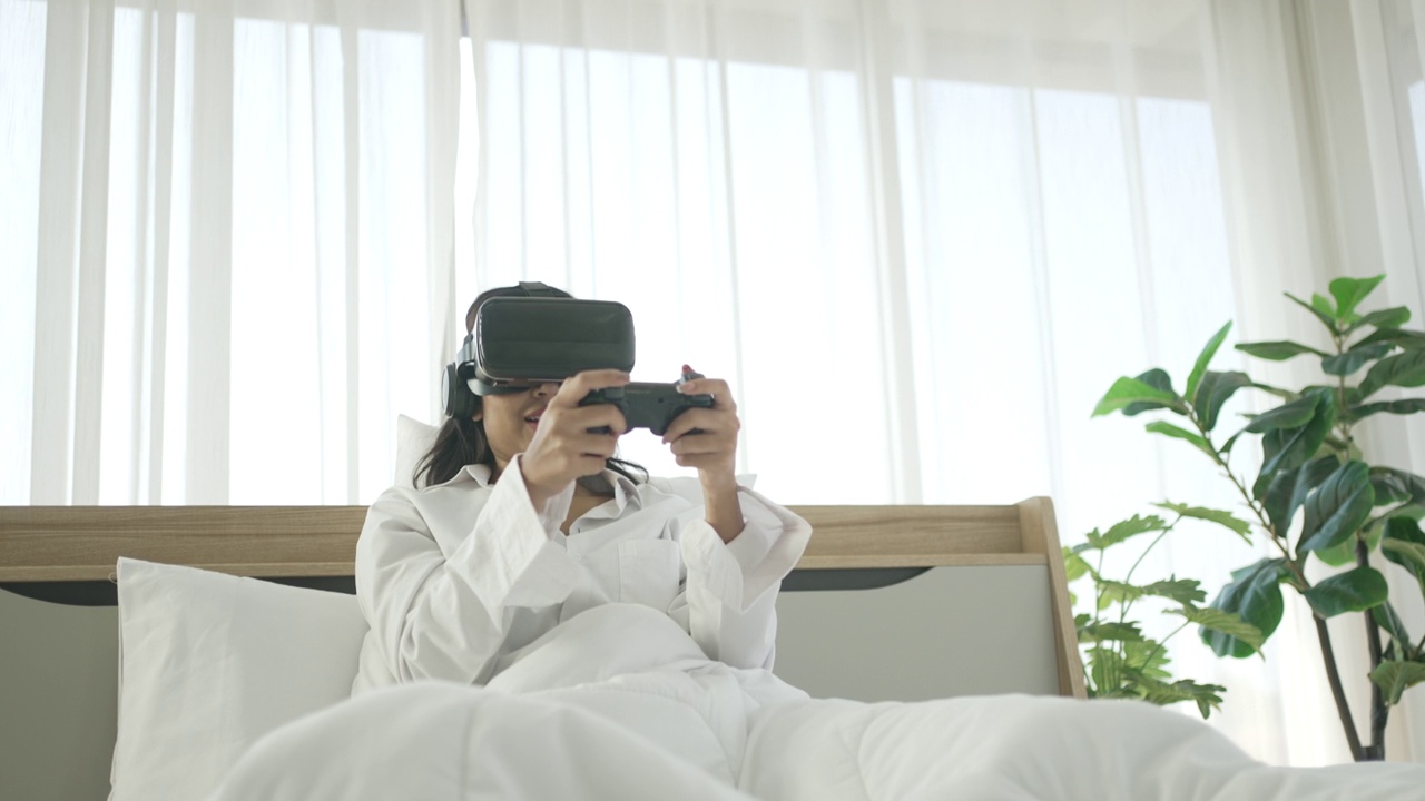 一名年轻女子戴着虚拟现实眼镜玩游戏。她呆在卧室里。视频下载
