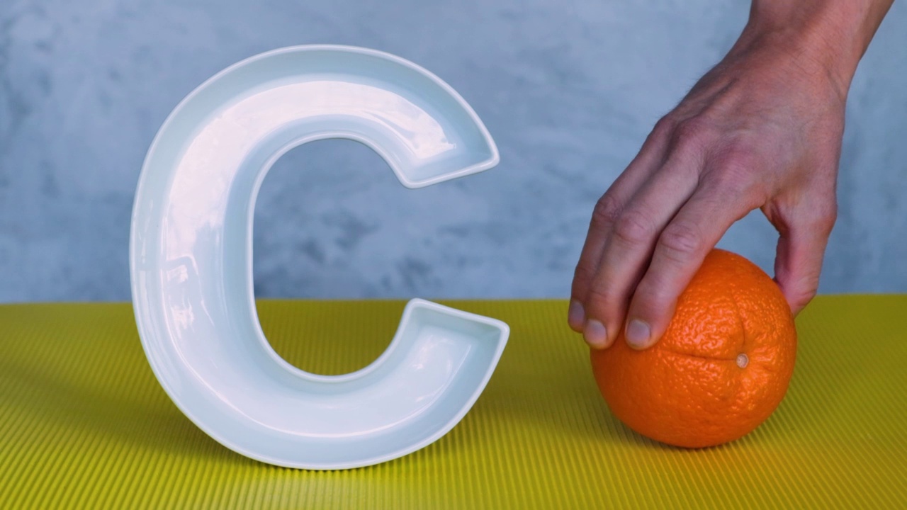 维生素C在饮食、饮食学上的概念。灰色和黄色的背景上字母C形状的盘子，人手把新鲜的橘子水果放在旁边。抗坏血酸对免疫系统功能很重要。视频下载