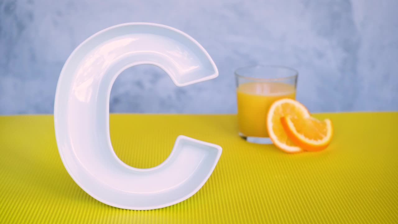食品中的维生素C，抗坏血酸概念。一名男子将可重复使用的金属吸管和鲜榨的橙汁放在大陶瓷字母C旁边的玻璃中。视频下载
