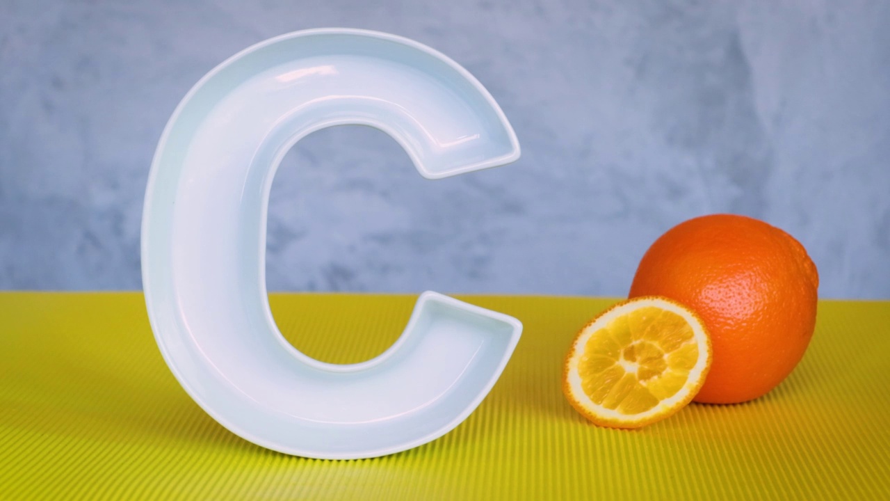 维生素C在食品中的概念。大大的陶瓷字母C，新鲜的橘子水果和橘子片掉在它前面。抗坏血酸对免疫系统功能很重要。视频下载