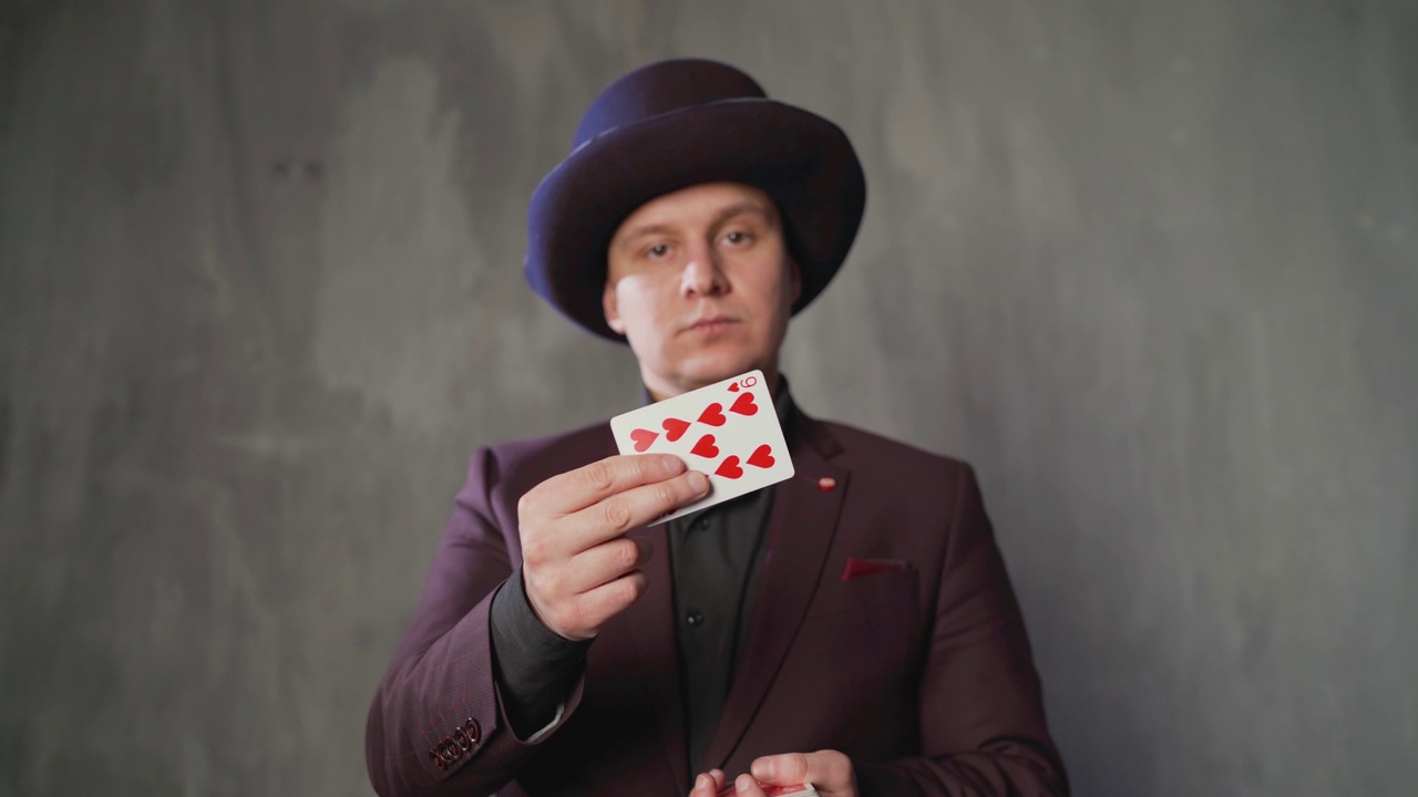 魔术师用纸牌表演魔术。男子魔术师的特写与两个扑克牌在他的手在灰色的背景。魔术师巧妙地换牌视频下载