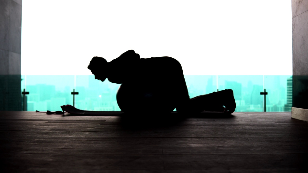 一个男人在健身球上伸展身体的剪影视频下载