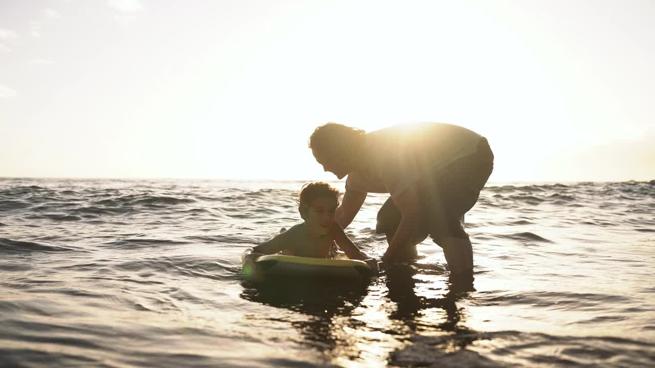 一个小男孩和他爸爸在沙滩上玩人体滑板视频下载