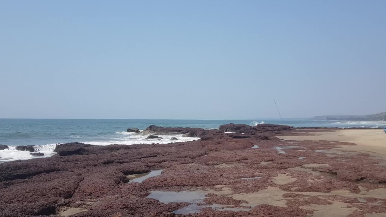 蔚蓝的天空，黑色的岩石和海浪拍打着海滩视频素材