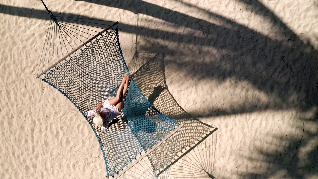上图中放松的女人在沙滩上的吊床上。视频素材