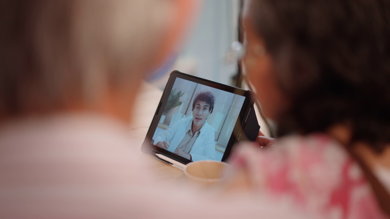 老年亚洲病人妇女正在协助成熟的成年男子与远程健康访问的笔记本电脑，而视频会议与男性医生视频素材