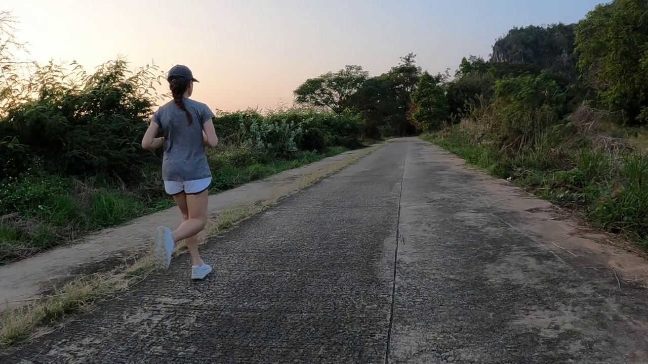 亚洲妇女在日落期间在公园的道路上跑步。视频素材
