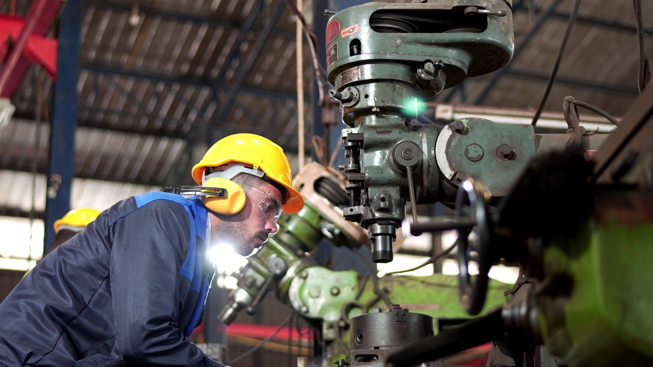 专业的工业工程师、技术员、工厂工人在安装时戴安全帽、安全眼镜，控制钻床重工业工厂。在制造工厂工作的员工。视频下载