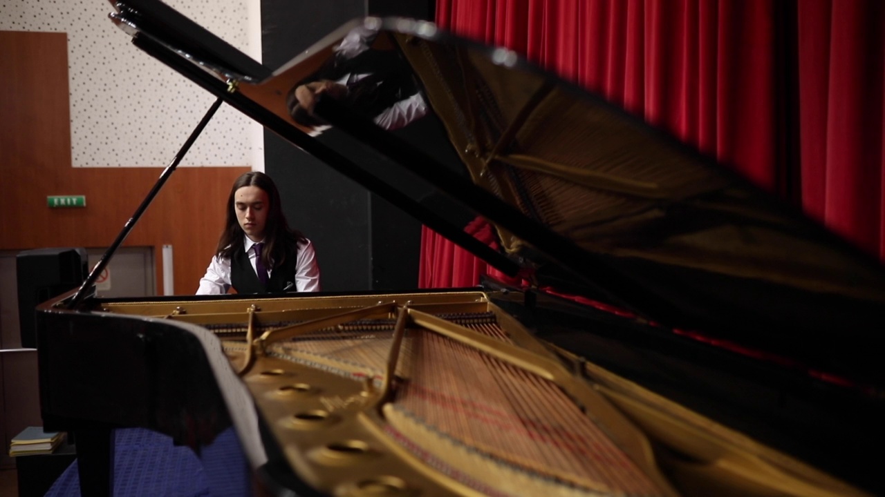 一位专注的年轻钢琴家在剧院里用三角钢琴演奏一首乐曲。视频下载