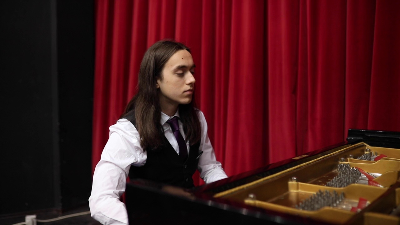 一位留着长发的天才钢琴家在观众面前练习演奏曲目。视频素材