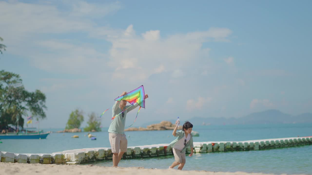 亚洲父亲和可爱的小儿子享受和快乐的假期活动，夏天在阳光下一起在美丽的沙滩上玩风筝，度假的生活方式旅行，家庭概念。视频下载
