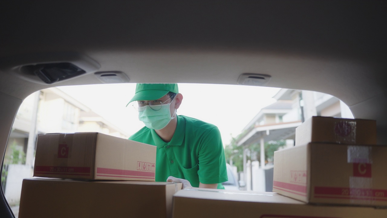 亚洲快递员穿着绿色制服，戴着防护口罩和医用橡胶手套，在客户家门口送一个纸箱给客户，分辨率为4k视频素材