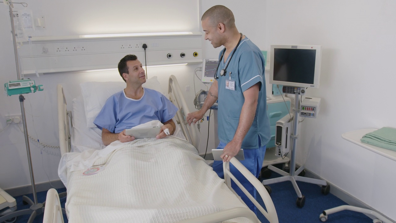 男护士在病床上与使用数码平板电脑的病人交谈视频素材