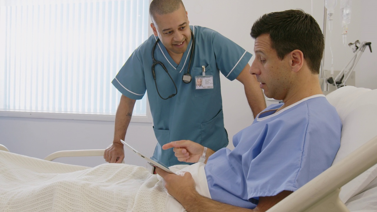 男护士在病床上与使用数码平板电脑的病人交谈视频素材
