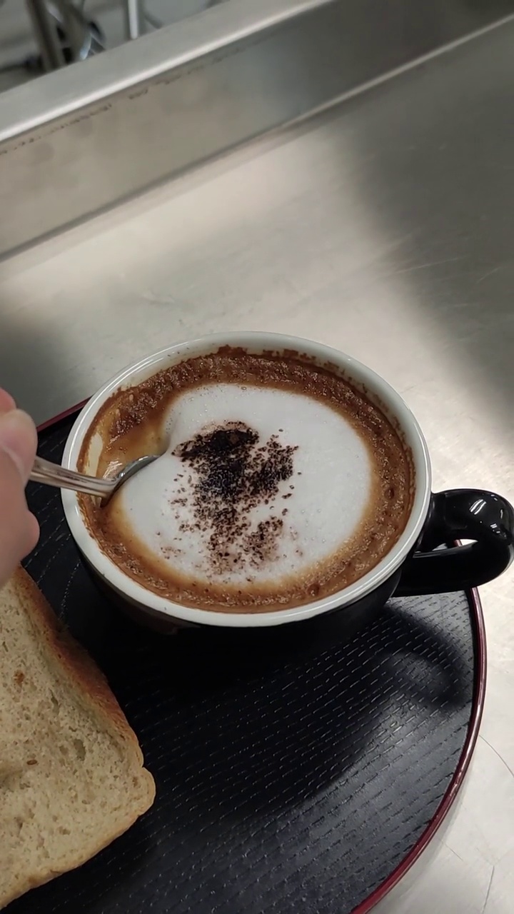 垂直视频特写镜头，早上的热咖啡拿铁艺术和面包。视频下载