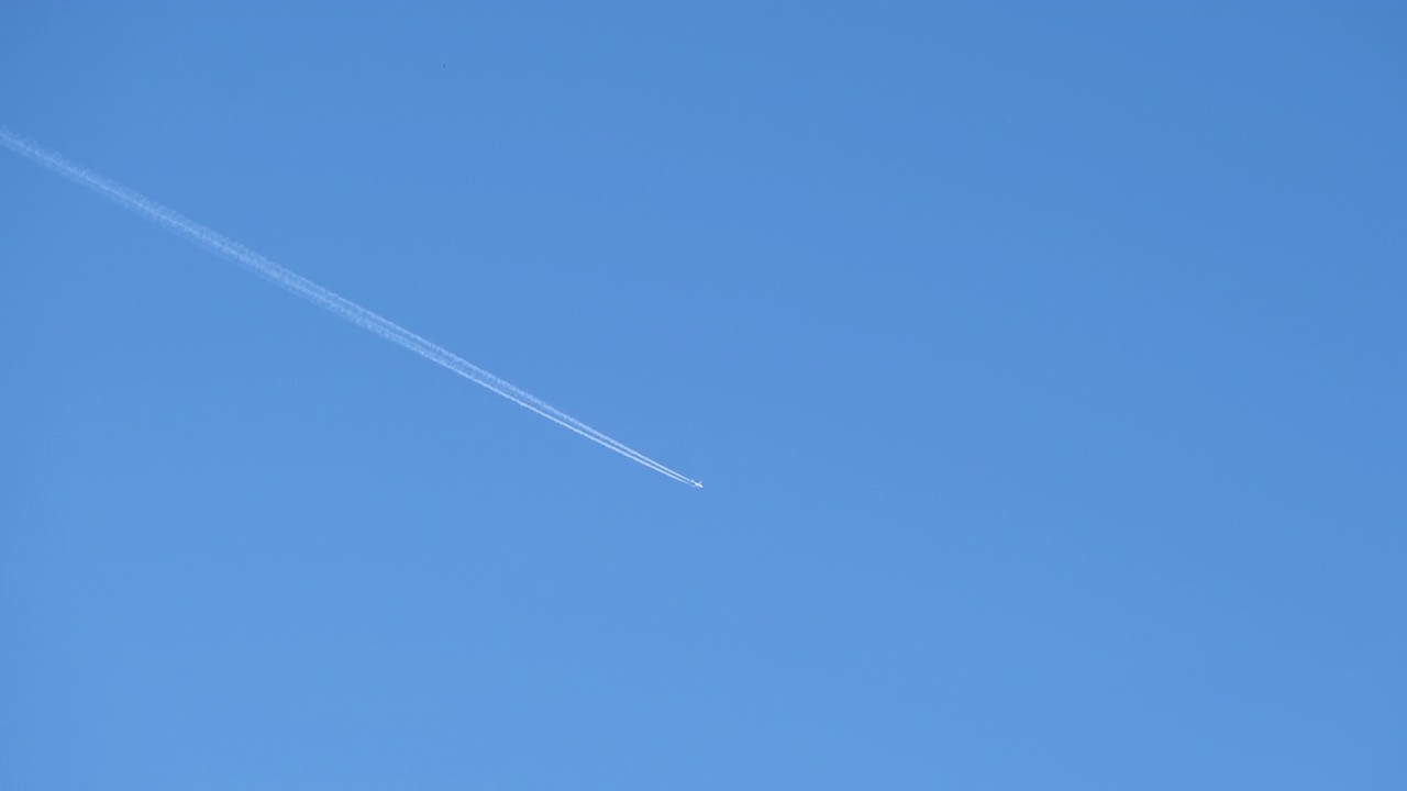 远处的喷气式客机在晴朗的蓝天上高空飞行，留下白色的烟迹。航空运输的概念视频素材