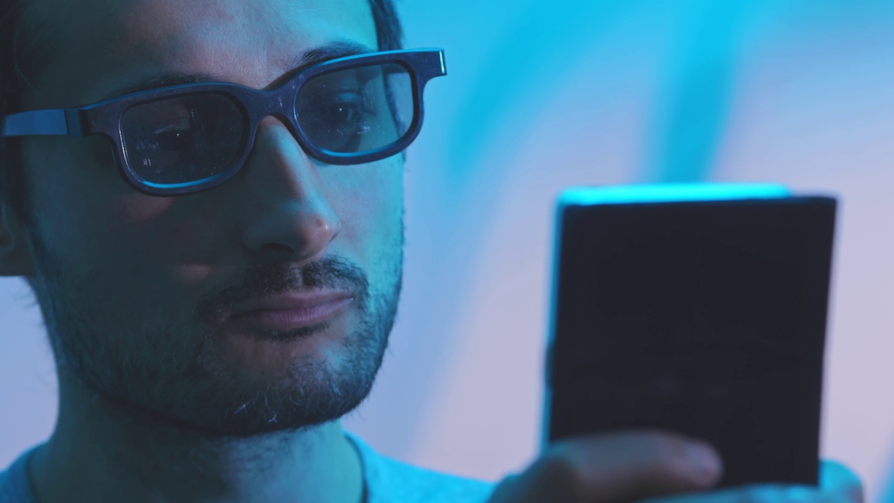 一名男子戴着3d眼镜看着智能手机显示器。增强的蓝色范围的配色方案视频下载