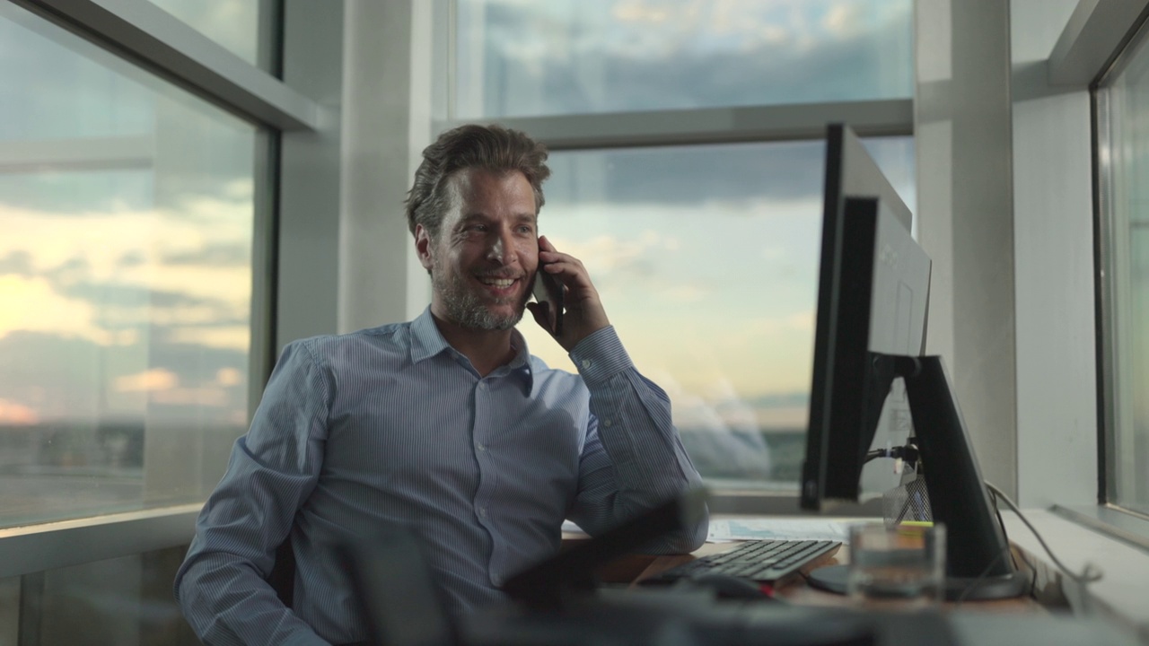 快乐的男企业家对着电话在电脑上工作，在家办公。视频素材