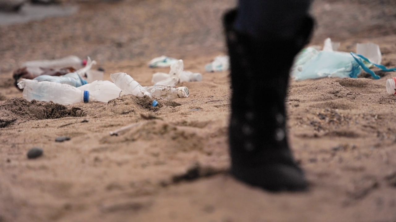 生态灾难。一个人在沙滩上走着踢起一个塑料瓶。低角度的观点。环境污染的概念视频素材