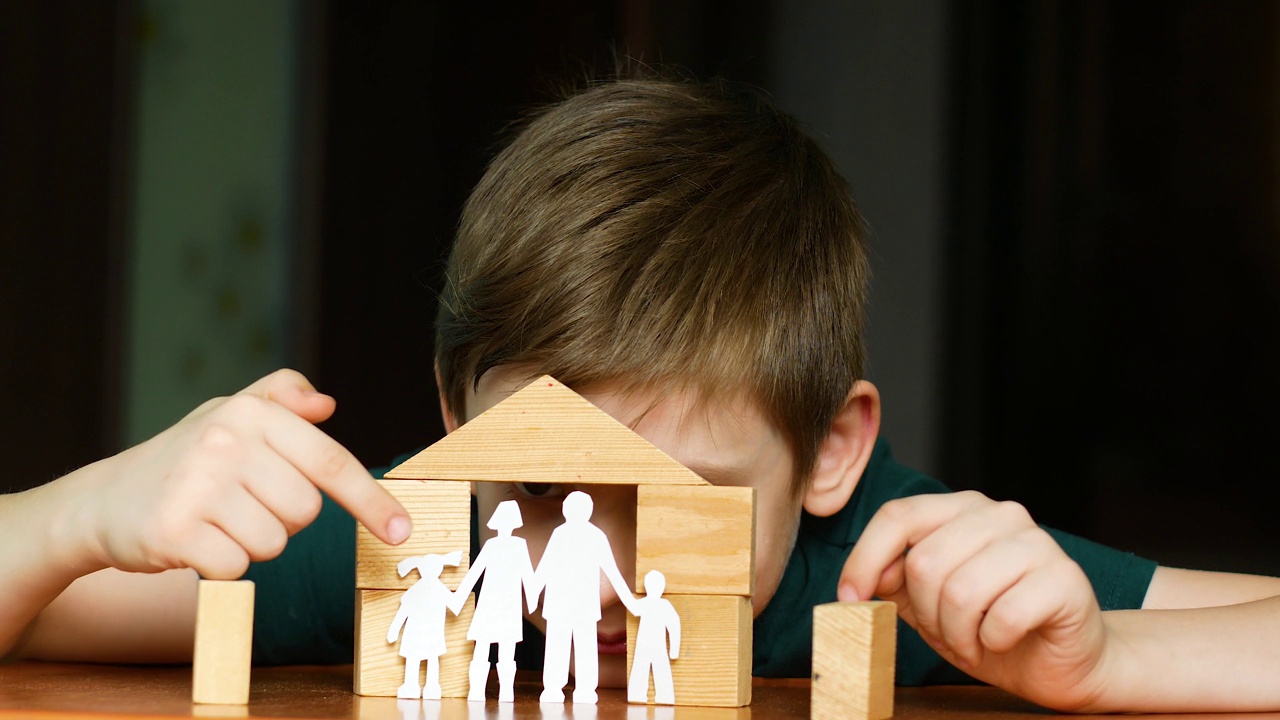 一名7岁的白人男孩玩着木头方块盖房子，孩子用纸剪出一个家庭。家庭的梦想。孩子对家和家人有着积极的梦想视频下载