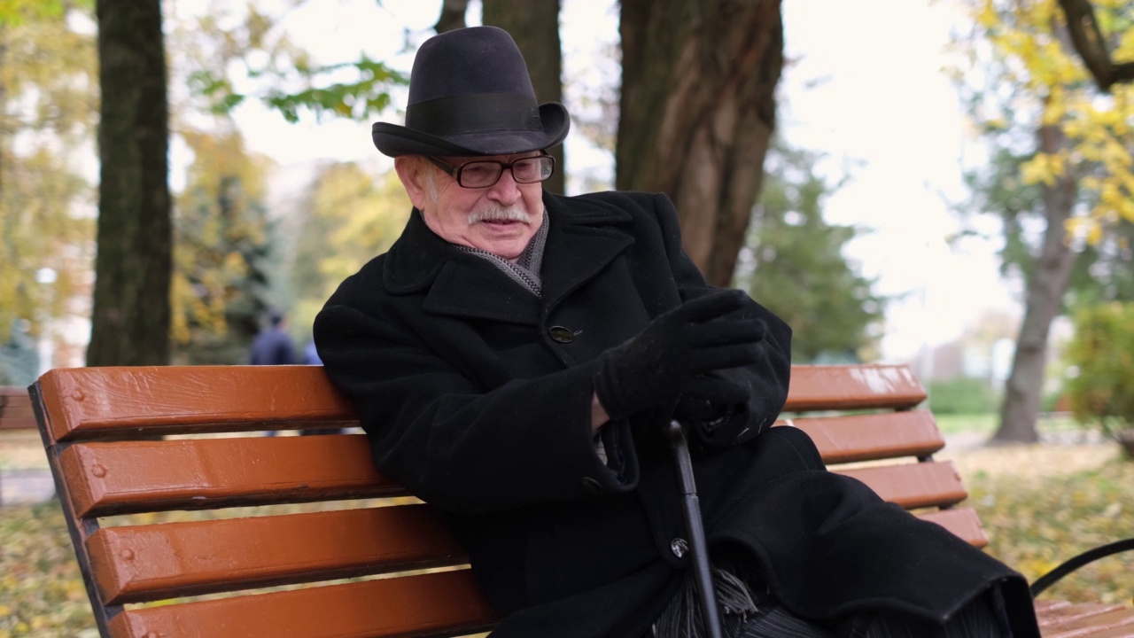 在一个寒冷的秋日，老爷爷坐在公园里。视频素材