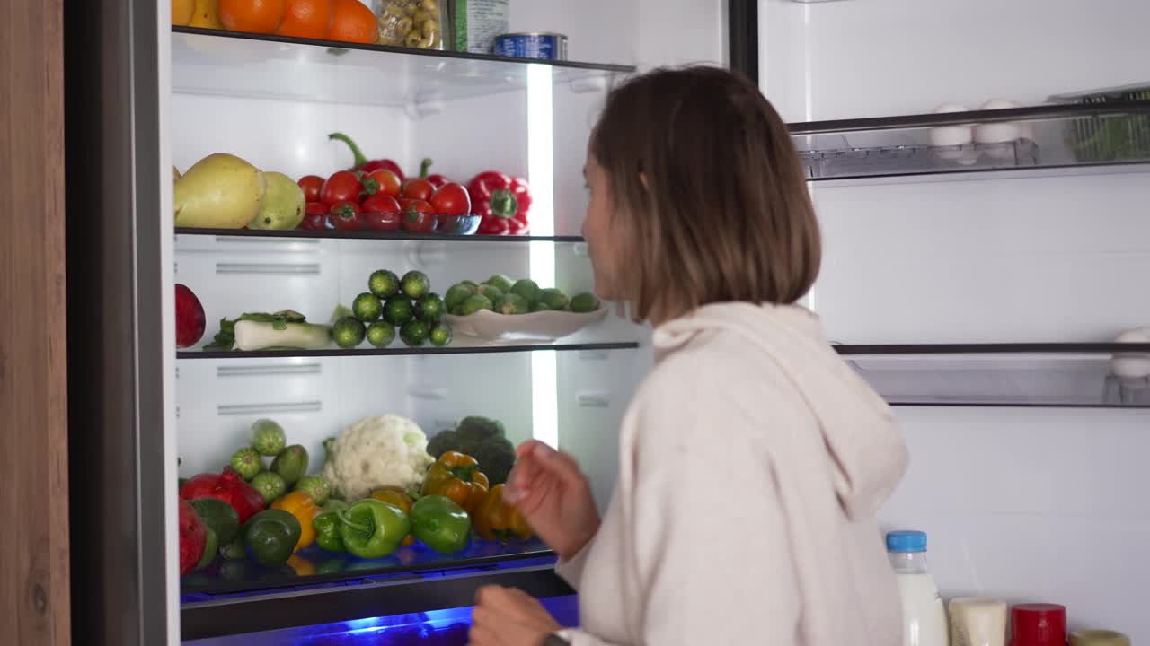 从冰箱里拿生食的女人。冰箱里装满了健康食品。水果和蔬菜。视频素材
