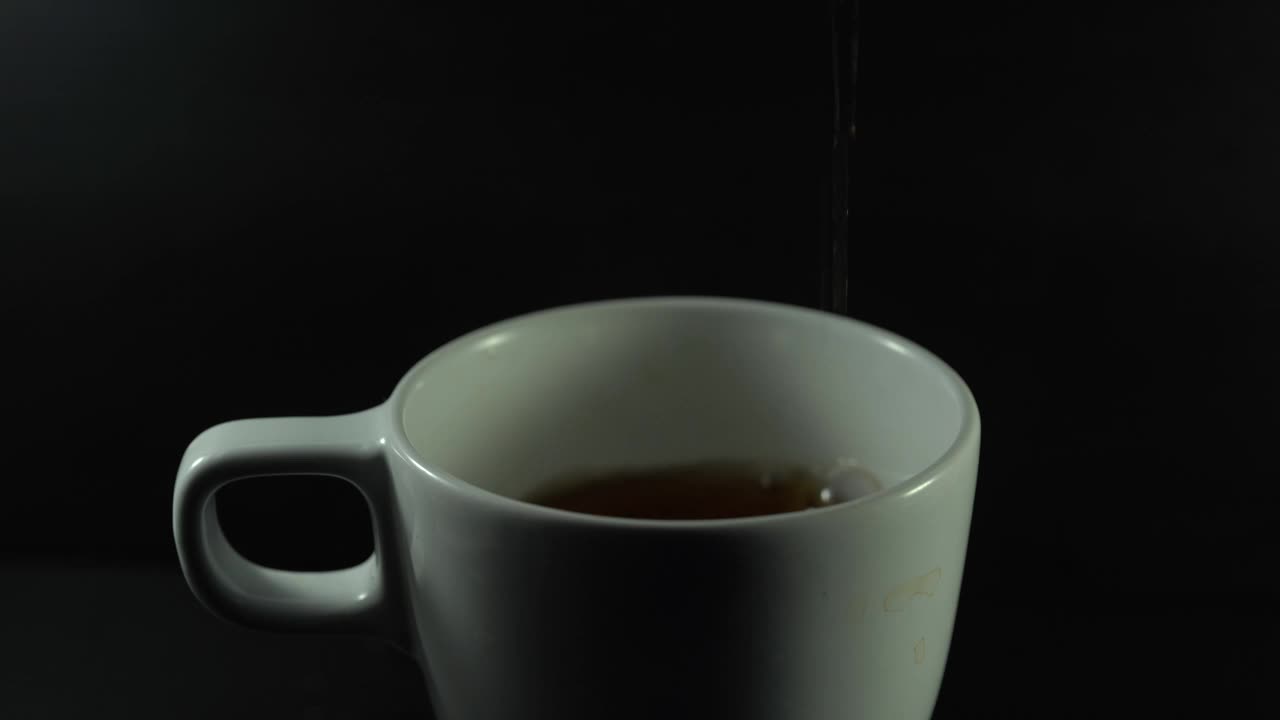 将茶从透明玻璃茶壶中倒入陶瓷茶杯中。视频下载
