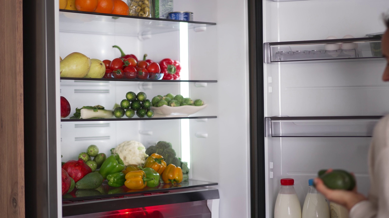 从冰箱里拿生食的女人。冰箱里装满了健康食品。水果和蔬菜。视频素材