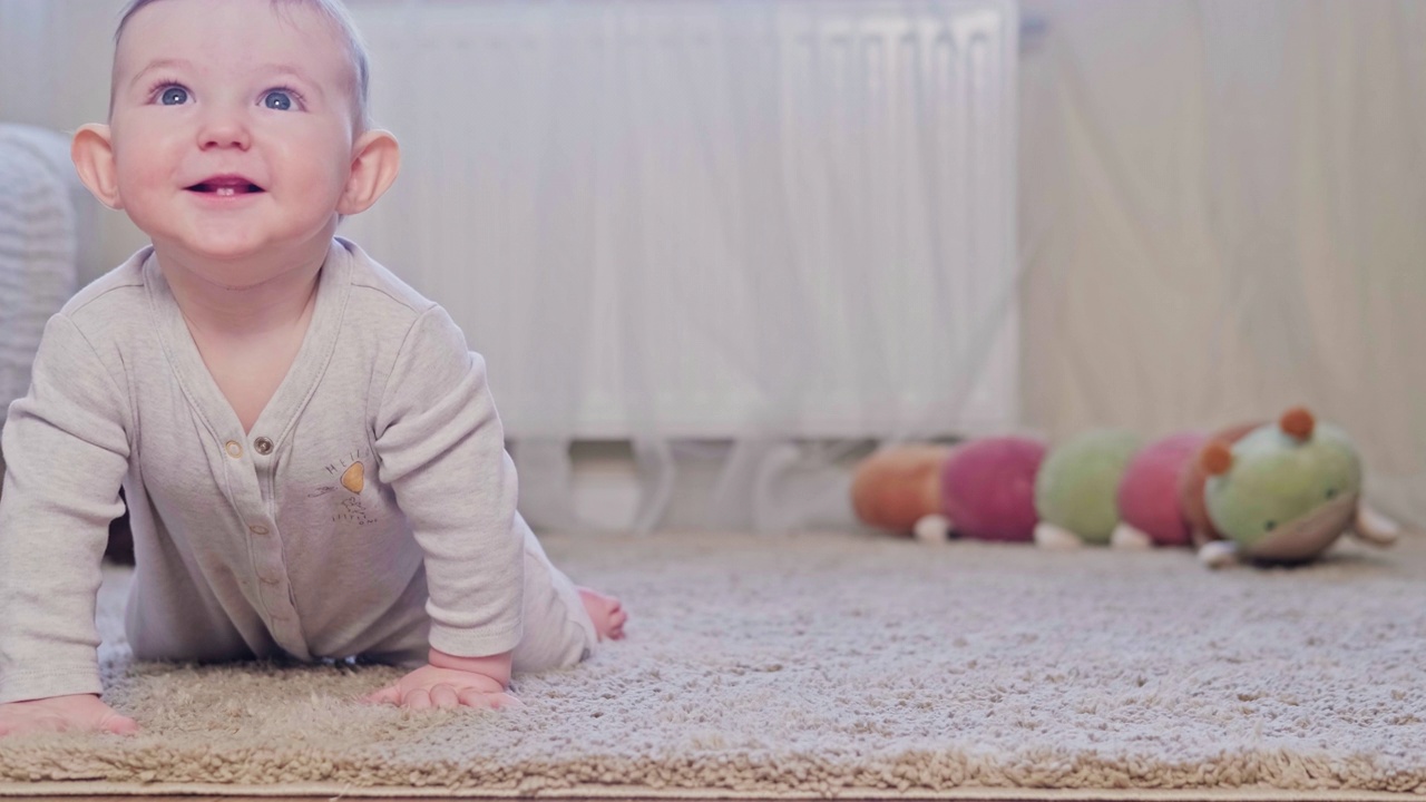快乐的孩子爬在保育室的地毯上。8个月大的小男孩带着玩具在地板上爬行视频素材