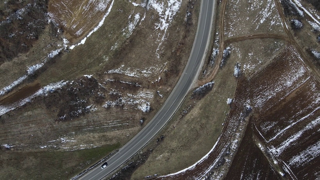 在塞尔维亚的尼斯，冬天的雪地里，一辆汽车行驶在蜿蜒曲折的山路上，高角度鸟瞰无人机拍摄的视频视频下载