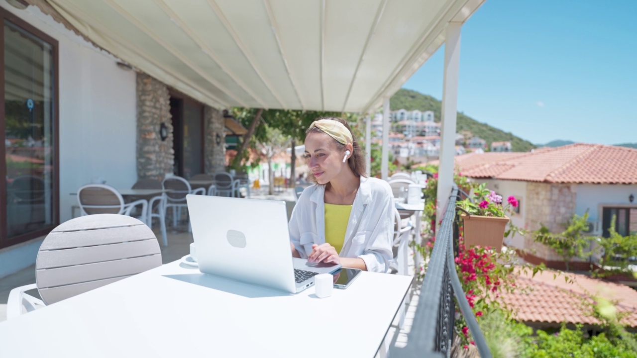 年轻的女商人自由职业女性在户外用笔记本电脑工作在白色开放的露台美丽的海景，在土耳其暑假期间远程在线工作，4k慢动作视频素材