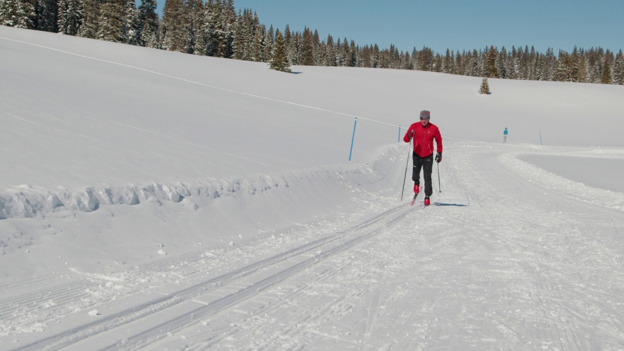 手持拍摄的越野滑雪者滑雪上山使用“经典，对角线步幅”的方法沿着一个整洁的小道在一个晴朗的一天，在科罗拉多州视频下载