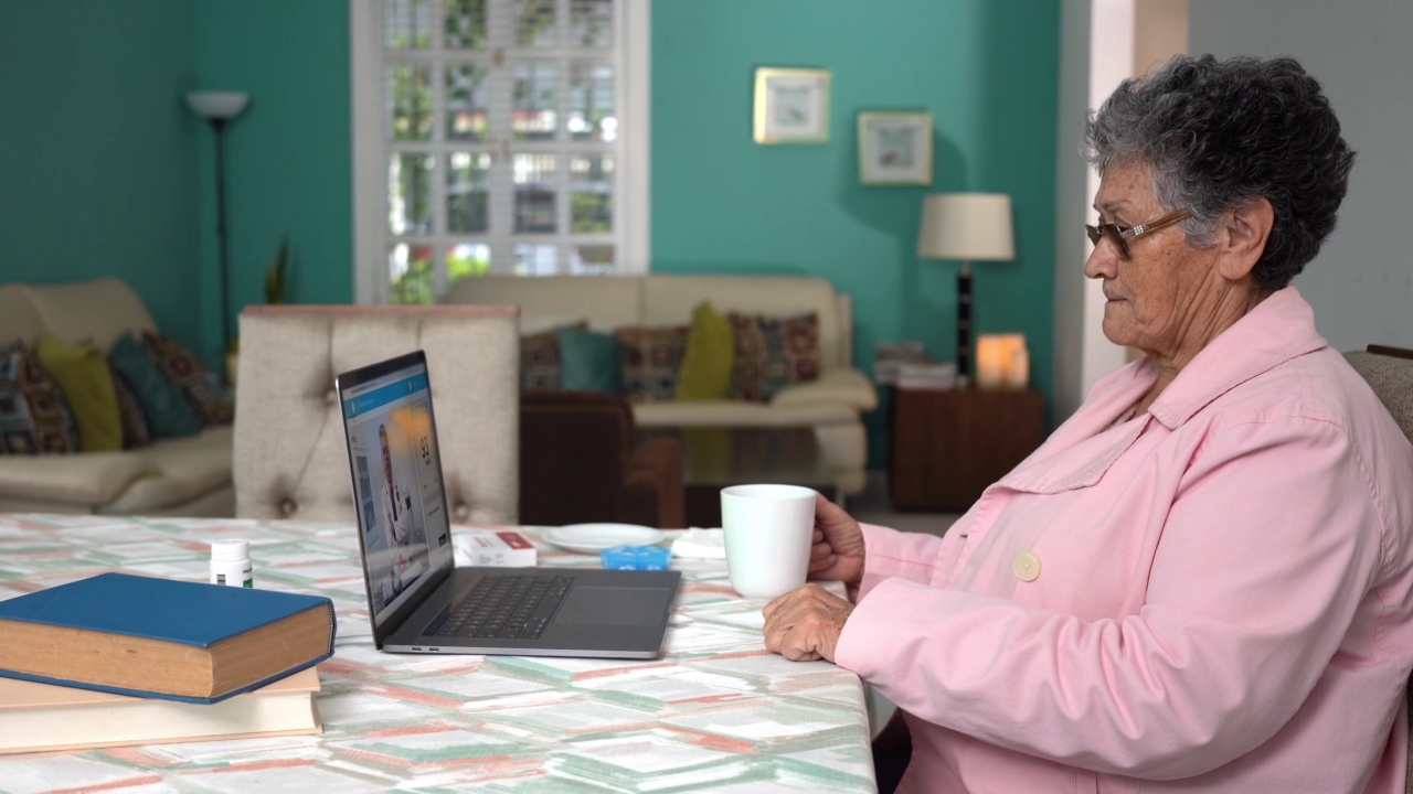 老太太在家拿着一杯茶，用电脑等着视频素材