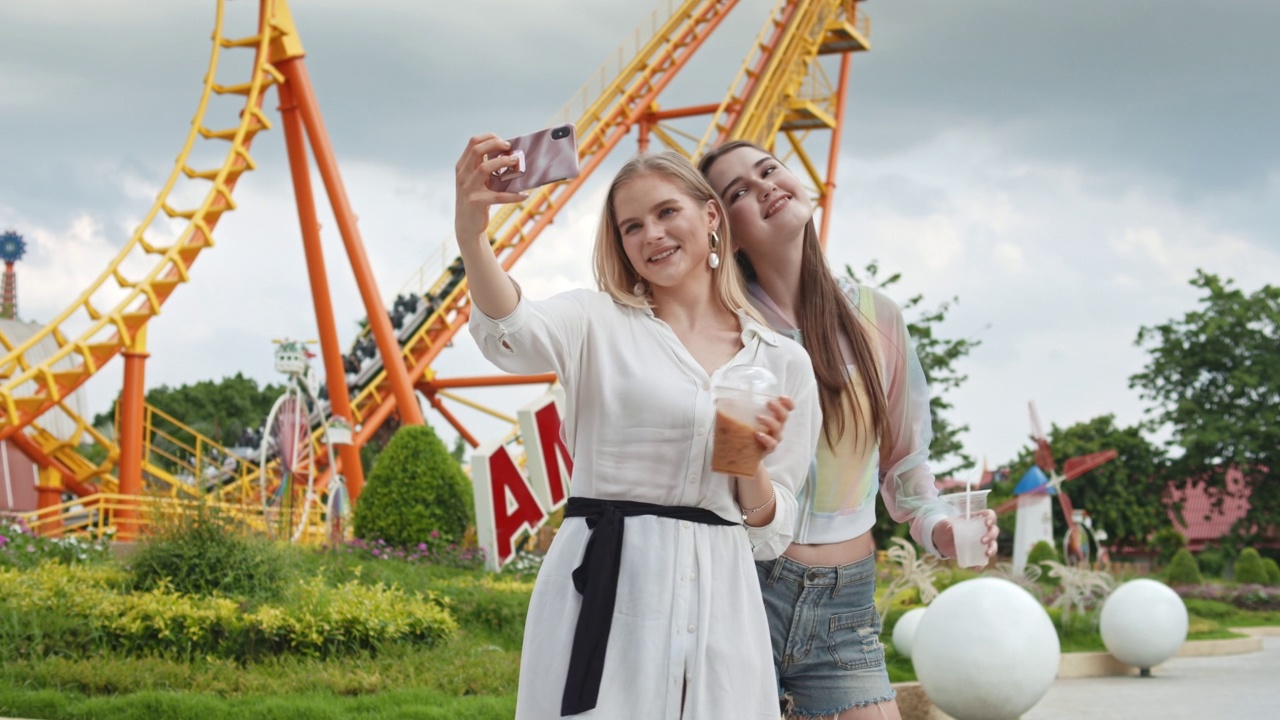 两个漂亮女孩在游乐园用智能手机自拍视频素材
