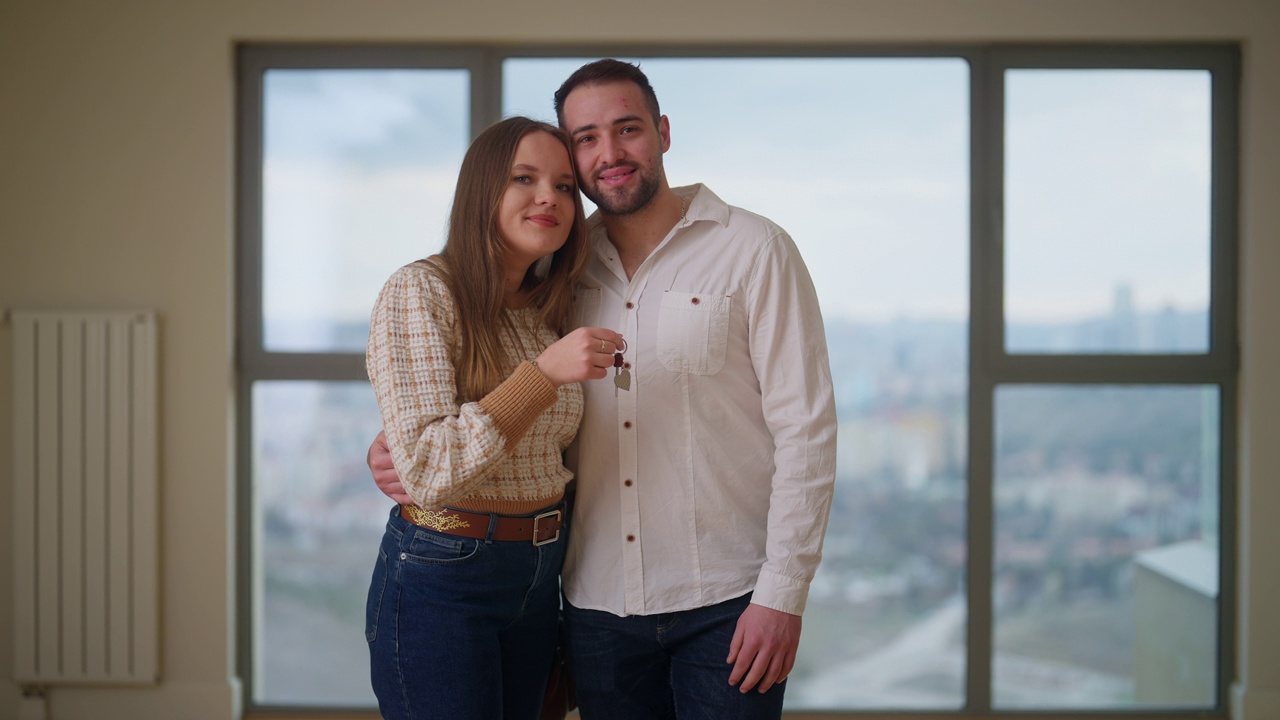 这是一对年轻夫妇在新家拿着钥匙，对着镜头微笑的照片视频下载