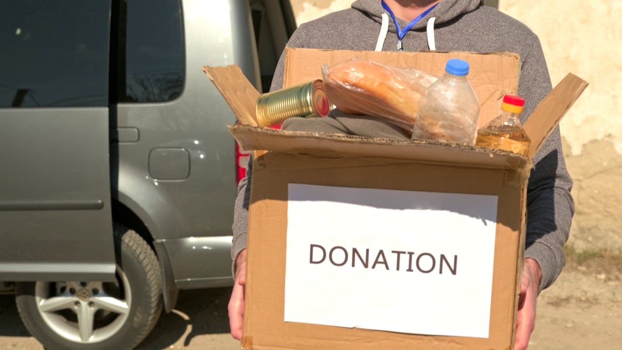 一名志愿者扛着装着食物和饮料的纸箱，准备给留在街上的难民。视频下载