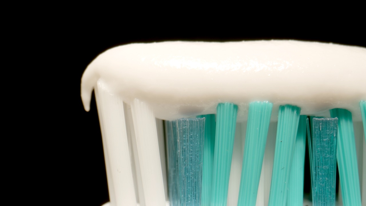 宏观:黑色背景的牙刷上的牙膏视频下载