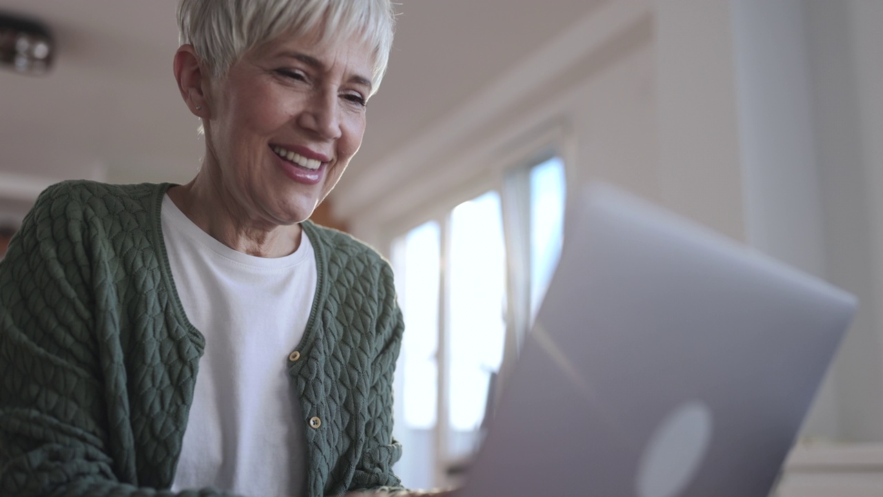 快乐的老女人在家里用笔记本电脑。视频素材