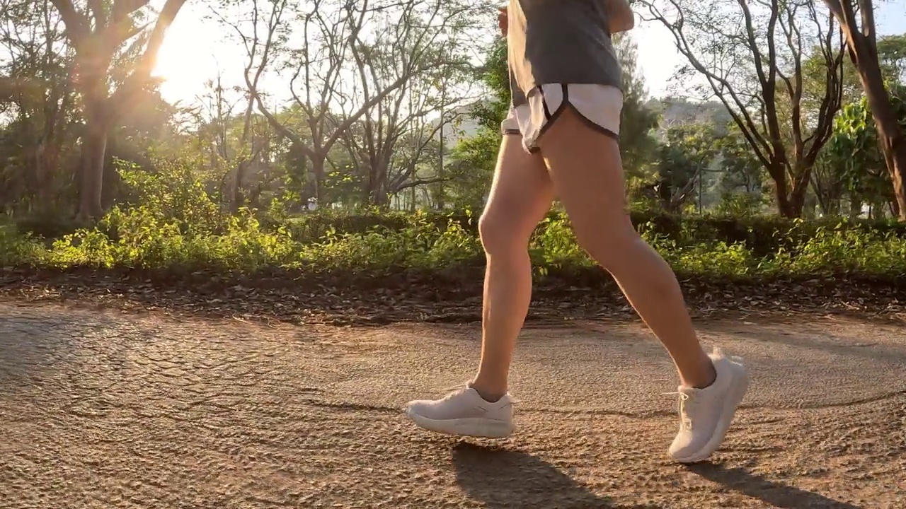 日落时分，在公园的马路上奔跑的女子的腿的慢镜头。视频素材
