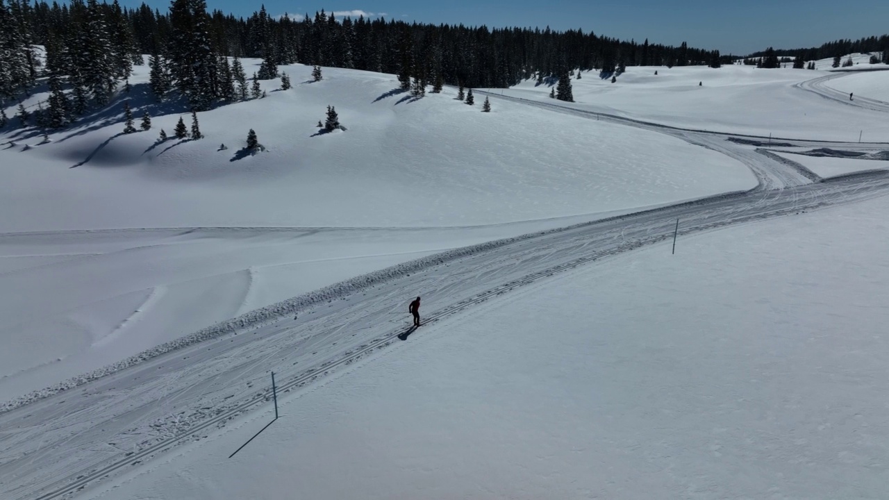 广角航拍一个越野滑雪者经典滑雪练习“踢双杆”方法在一个清晰，阳光明媚的“蓝鸟”日在科罗拉多的Grand Mesa国家森林经过修整的小道视频下载