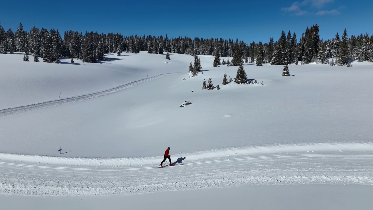 一个越野滑雪者滑雪和练习“对角步幅”方法的广角航拍在科罗拉多的Grand Mesa国家森林的修整小径上视频下载