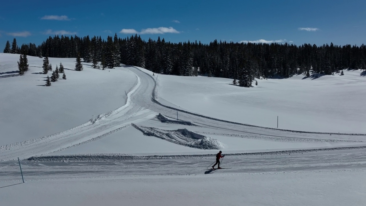 广角航拍越野滑雪者滑雪和练习“对角线步幅”方法在一个清晰，阳光明媚的“蓝鸟”日在科罗拉多的Grand Mesa国家森林经过修整的小道视频下载